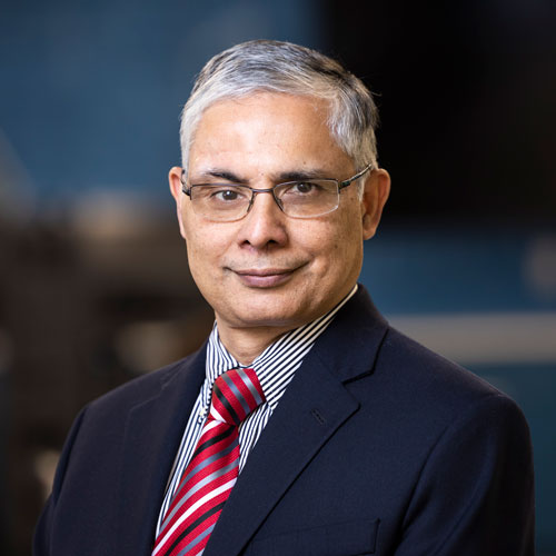A headshot of School of Computing dean Gurdip Singh wearing a navy suit jacket, a light blue shirt and a striped red tie.